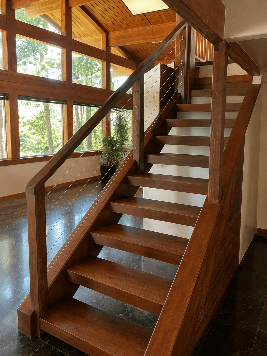 An open-riser wood staircase with refinished treads and a stainless cable railing in a timber-framed room.