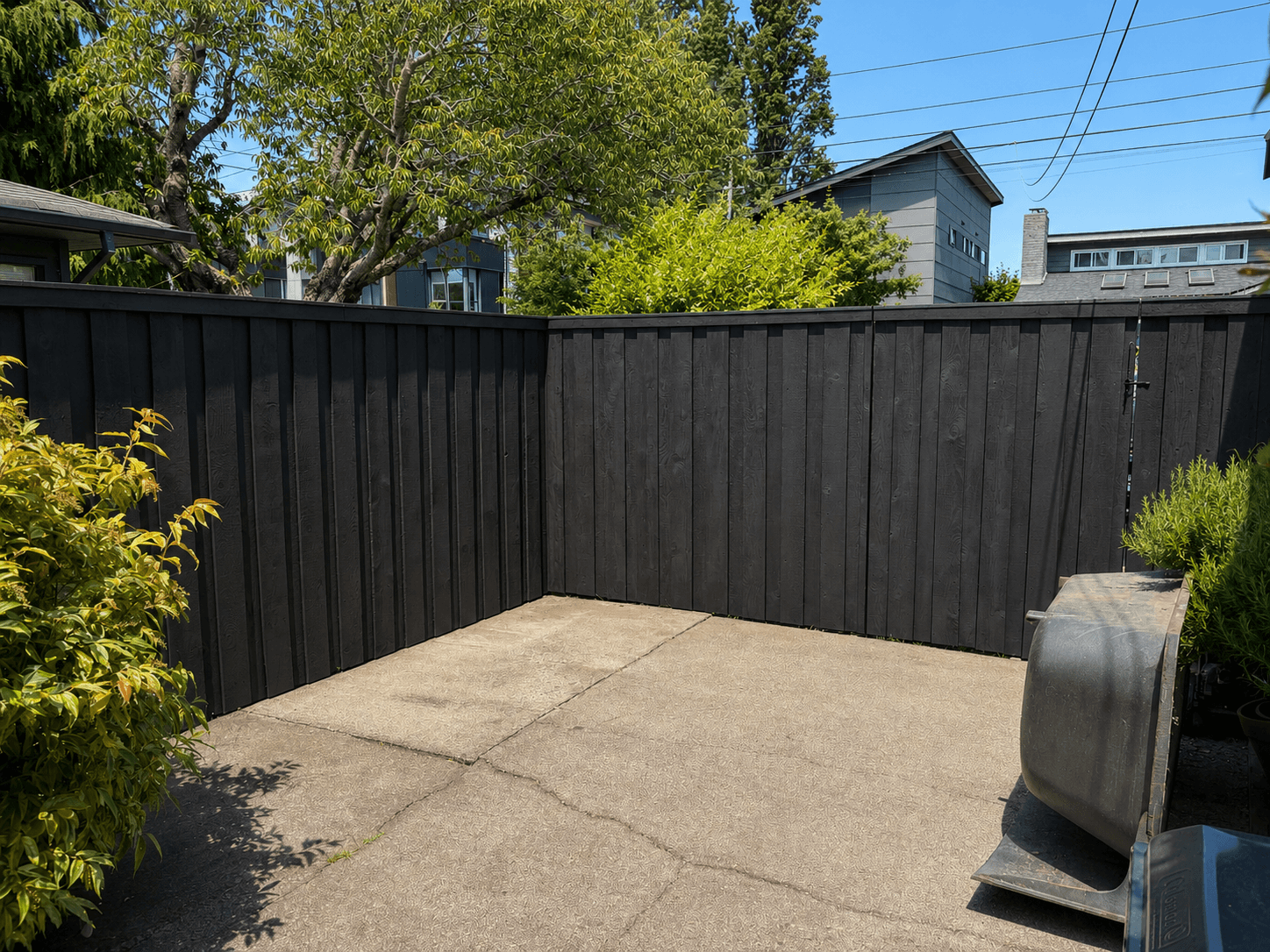 A black-stained vertical board fence wrapping a private concrete patio corner with layered greenery.