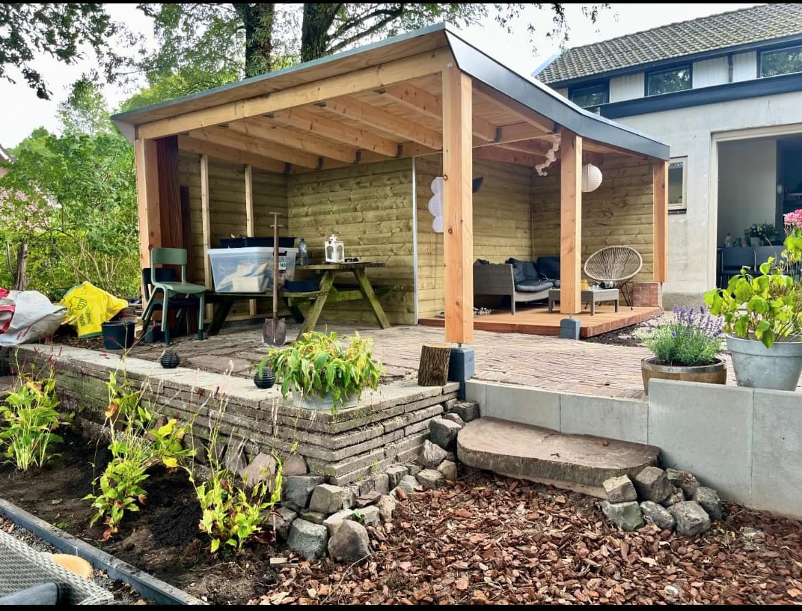 A cedar garden pavilion with a standing-seam roof over a brick patio, set on a stone-edged planting bed.