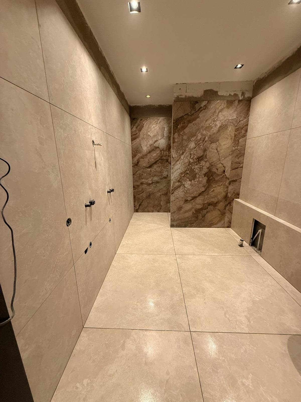 A bathroom clad in large-format travertine tile with a book-matched brown marble feature wall.
